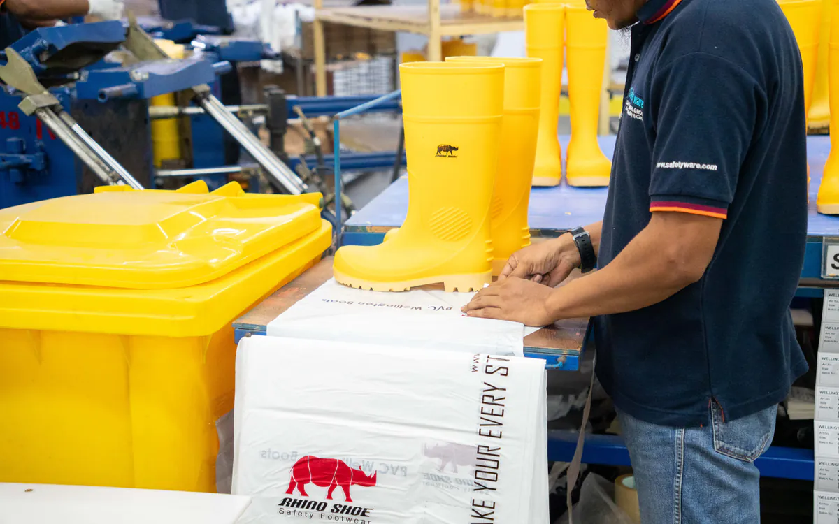 RHINO SHOE team member completing final checks and packing yellow PVC safety boots